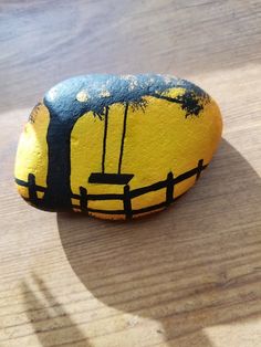 a painted rock sitting on top of a wooden table next to a tree and fence