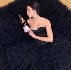 a woman in a black dress holding an award while sitting on the floor with her legs crossed