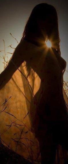 a woman standing in tall grass with the sun shining through her hair and arms behind her back