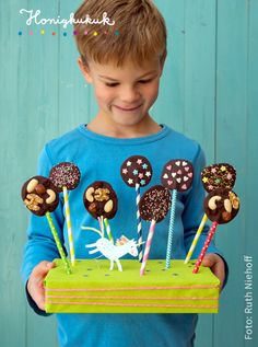 a young boy holding up a cake with chocolate and sprinkles on it