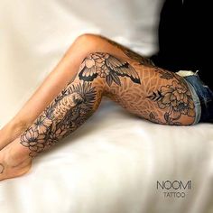 a woman's legs with tattoos on them sitting on a white bedding sheet