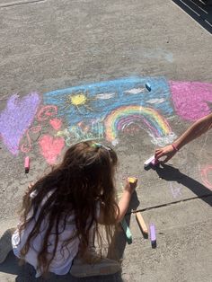 two girls are drawing on the sidewalk with chalk