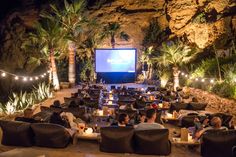 an outdoor movie theater with people sitting in chairs and watching the movies on large screen