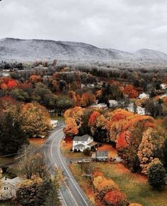 an aerial view of a road surrounded by trees with fall foliage on the mountains in the background