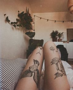 a woman's legs with tattoos on them laying in bed next to a potted plant