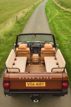 the back end of a brown and tan car parked in front of a green field