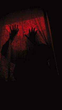 the shadow of two hands reaching out from behind a curtain in front of a red light