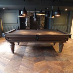 a pool table in the middle of a room with several lamps hanging from the ceiling