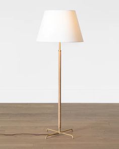 a floor lamp with a white shade on the base and a wooden stick in front of it