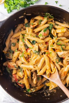 pasta with chicken and spinach in a skillet on a white counter top next to parsley