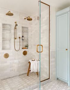 a white tiled bathroom with gold fixtures and glass shower doors, along with an open shelf