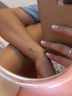 a woman's hand with a small cross tattoo on her left wrist, in front of a mirror