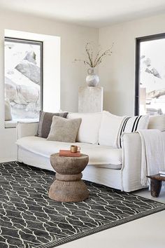 a living room filled with white furniture and large windows next to a black area rug