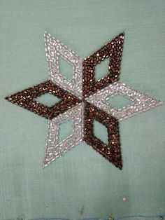 an embroidered snowflake is shown on a green cloth with silver and brown sequins