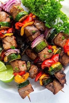 skewered meat and vegetables on a plate with lime wedges