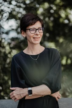 a woman wearing glasses standing with her arms crossed