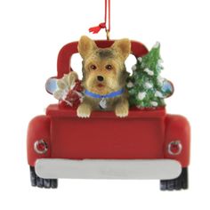 a christmas ornament with a dog sitting in a red toy car holding a small tree