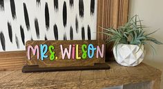 a wooden sign that says mrs wilson next to a potted plant on a table