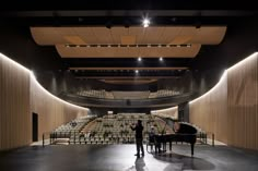 two people standing in front of a piano and an auditorium full of seats with lights on the ceiling