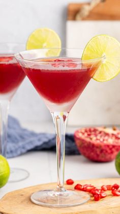 two glasses filled with red liquid and garnished with limes on a cutting board