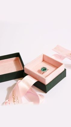 an open box with a ring in it and pink ribbon on the side, sitting next to two other boxes