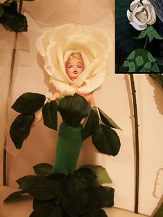 there is a doll with a flower in the middle of it's head and on top of some fake flowers