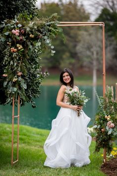 a woman in a wedding dress standing under an arch with greenery and flowers on it