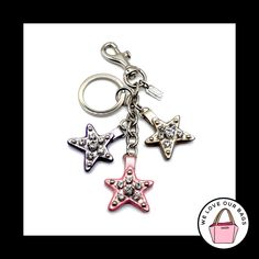 three star shaped key chains are shown on a white background with a pink purse in the foreground