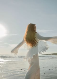 a woman standing on top of a beach next to the ocean holding her arms out