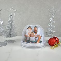 a snow globe with an image of two people under it and christmas trees in the background