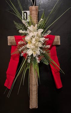 a cross decorated with white flowers and greenery on a black wall behind a red table cloth