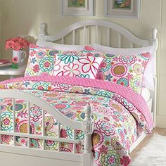 a white bed with pink and green flowers on the comforter is next to a window