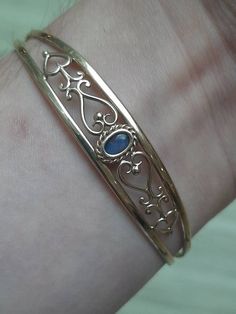 A vintage 9ct gold black opal doublet bangle. The bangle is Hallmarked 9ct gold. The black opal doublet is set at the centre and measures 6 x 4mm's. It is then flanked on both sides by a heart pattern that has been cut in to the gold. This bangle is flexible so it can easily be put on, and taken off of the wrist.