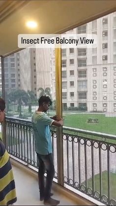 two men are standing on a balcony looking out at the grass and buildings behind them