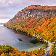 an aerial view of a lake surrounded by trees in the fall with orange, yellow and green foliage