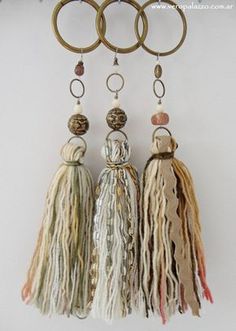 three tasseled key chains hanging from a hook on a white wall next to two rings