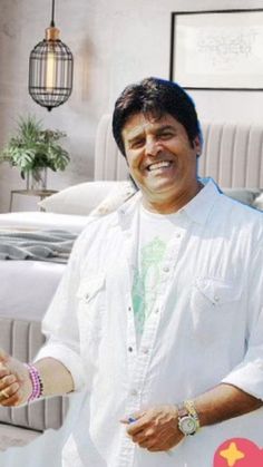 a man standing in front of a bed with his hand out to the side and smiling