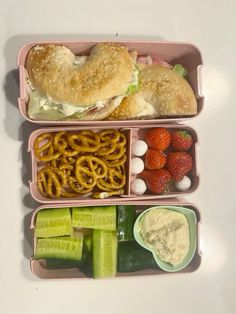 two pink containers filled with food sitting on top of a white table next to strawberries and cucumbers