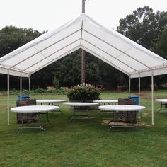 a white tent with tables and chairs under it on the grass in front of some trees