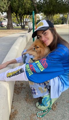 a woman holding a small dog sitting on top of a cement bench next to a park