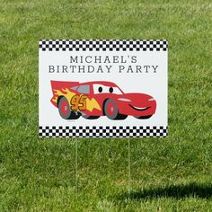 a birthday party sign in the grass with a race car on it's side