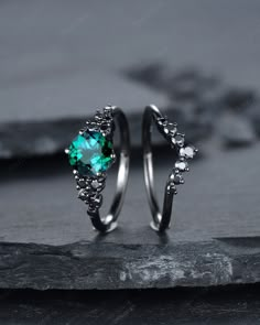 two silver rings with green stone in them on top of a slate slab, next to each other