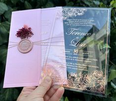 a person holding up a pink and blue wedding card with a flower on it's side