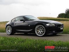 a black bmw z4 parked on the side of a road in front of tall grass