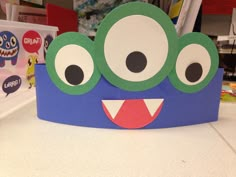 a paper crown with googly eyes and mouth on a table in front of children's books