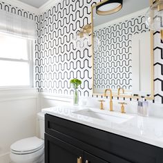 a bathroom with black and white wallpaper, gold fixtures and a large mirror over the sink