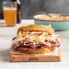 a roast beef sandwich with coleslaw and slaw on a cutting board next to a glass of beer