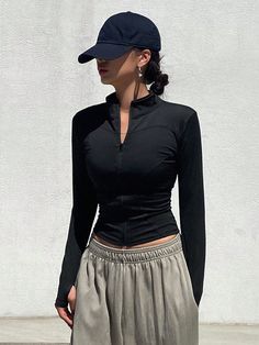 a woman standing in front of a white wall wearing a black top and grey skirt