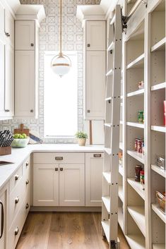 a kitchen with white cupboards and shelves filled with food, drinks and other items