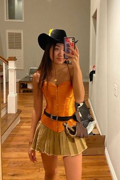 a woman taking a selfie with her cell phone wearing a cowboy hat and gold skirt